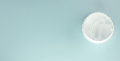 White cosmetic face cream in a round open jar on a light blue background, top view, copy of the space on the left