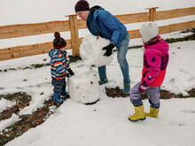 Father Helps To Build A Snowman With Children