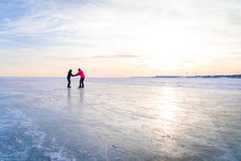 Boy Helping Mom Skate On Frozen Lake In Winter At Dusk