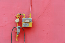 A Yellow Gas Meter Attached To The Pink Wall.