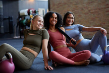 Smiling Women Sitting With Weights On A Gym Floor