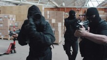 A police swat team searches a warehouse with guns drawn wearing balaclavas an gas masks