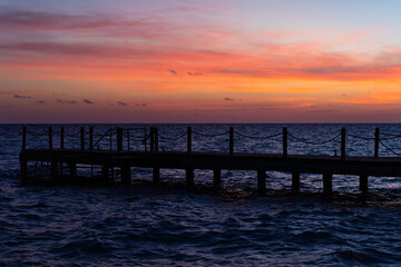 Wall Mural - Rope bridge silhouette at sunset. Beautiful seascape, bright orange sky and sea