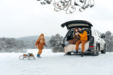 Winter portrait of a family sit on car trunk enjoy their vacation in forest