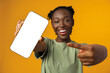 © fotofabrika - Young smiling african american woman showing smartphone with blank screen against yellow background
