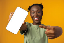Young Smiling African American Woman Showing Smartphone With Blank Screen Against Yellow Background