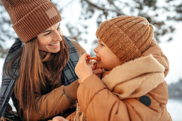 Wall Mural - Young woman with a son in winter forest on a picnic drink hot tea