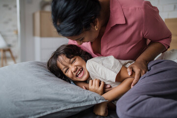 Wall Mural - Happy mother tickling her little son when waking him up in morning.