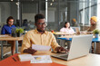 © Mediaphotos - Concentrated young Black analyst in eyeglasses sitting at table and using laptop while examining papers in coworking space