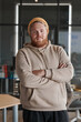 © Mediaphotos - Portrait of smiling young bearded Caucasian man in hat and hoodie standing with crossed arms in office