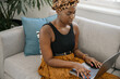 © JonoErasmus - Gen z Black African woman sitting on sofa at home typing on laptop