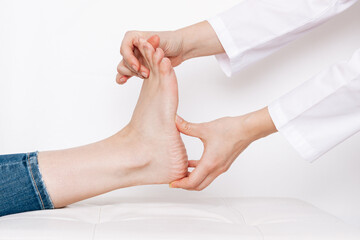 Examination of a young woman by an orthopedist. Cropped shot of female doctor in a white coat holding a girl's foot in her hands. Flat feet, injury. Foot treatment. Pain from uncomfortable shoes