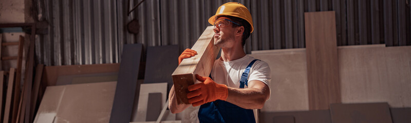 Wall Mural - Handsome young man carrying wooden plank at construction site