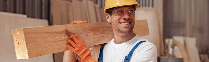 Wall Mural - Cheerful worker carrying timber wood plank at construction site