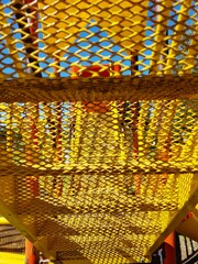 Puente de acero amarillo con entramado de panal en el parque infantil, forma un hermoso diseño abstracto con un fondo de la torre en bokeh