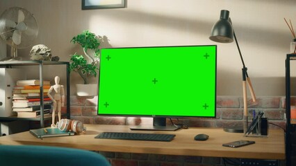 Fototapete - Desktop Computer Monitor Standing on a Desk with a Green Screen Chromakey Mock Up Display. Cozy Empty Loft Apartment with a Lamp, Notebooks and Smartphone on the Table. Zoom In Shot.