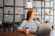© dikushin - Portrait of tired thinking young business woman sitting at desk with laptop in modern office room, holding cup with coffee, looking away. Pretty Caucasian lady remote working or studying at workplace.