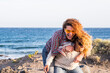 Couple of young adult woman having fun carrying in piggyback and laughing a lot. Curly hair female people enjoy leisure activity outdoor with ocean in background. Summer holiday vacation lifestyle