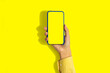 © Home-stock - Social network and modern technologies. A woman's hand holds a phone with a blank screen on a yellow background, close-up, a place to copy