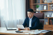 © Liubomir - Accountant-auditor works in a classic office, calculates financial reports, Asian businessman works with computer and documents, paperwork