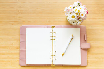 Wall Mural - Flat lay, top view of a pastel pink diary flower bouquet and stationery on a wooden desk.