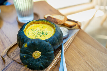 Roasted pumpkin cream soup in raw pumpkin serve with bread on rustic wooden background.