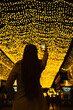 © Dina - woman at night taking a picture on mobile phone camera of golden yellow lights in the street in city, real people using technology and mobile photography hobby