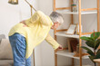 © Pixel-Shot - Senior woman with back pain taking book from shelf at home