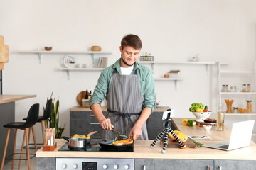 Canvas Print - Young man cooking vegetables from video tutorial in kitchen