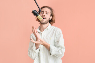 Canvas Print - Handsome young man singing in microphone on color background