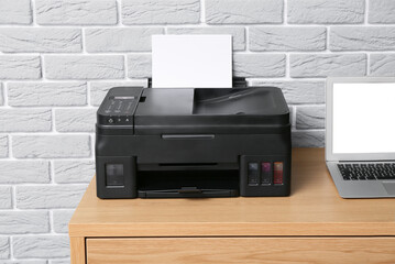 Workplace with modern laptop and printer near grey brick wall, closeup