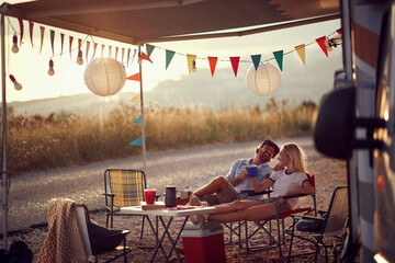 Wall Mural - Couple sitting  in front of camper van and drinking .Travel and friendship celebration concept