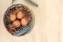Easter Eggs In A Basket Of 4 With Pine Leaves And Pine Cones On A Light Wooden Background.