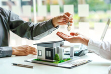 The Real Estate Agent Gives The Buyer The House Keys On A Table With Modern Miniature House Model.