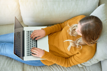 Wall Mural - Connected to the world from the comfort of home. High angle shot of a young woman using her laptop while sitting on the sofa at home.