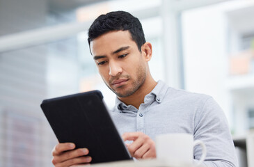 Canvas Print - Always stay informed. Shot of a young businessman drinking coffee while using his digital tablet.