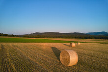 3 Straw Bales On Agricultural Field After Wheat Harvest. Hills Of The Swabian Alb In The Background Against A Blue Sky. Aerial View. Germany.
