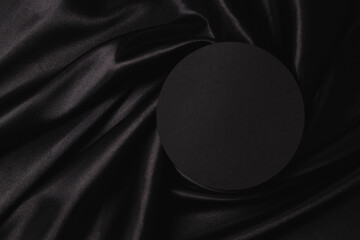Empty round platform podium on beautiful black color background with drapery and wavy folds of silk satin material. Mock up monochrome background for cosmetic product presentation. Top view