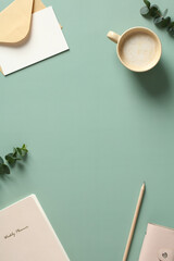 Wall Mural - Vertical banner of home office desk table with cup of coffee, paper notebook, eucalyptus leaves. Flat lay, top view.