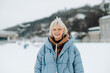 © bodnarphoto - Smiling girl with blond hair in warm winter clothes on a walk posing for the camera on a background of snowy views.
