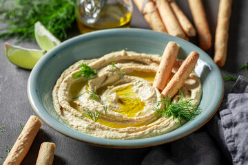 Tasty and homemade hummus with breadsticks, olive oil and dill.