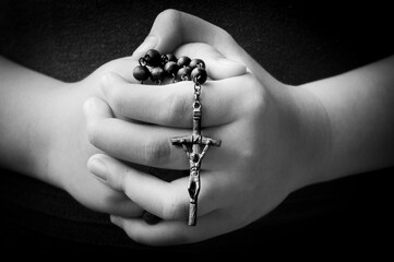 Child hand holding Holy Rosary - Black and white background. Religious concept