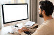 © Vadim Pastuh - Back view of positive Hindi man in smart casual clothes using computer while sitting at the desk in his flat. Young Indian male student watching webinars, educational courses, learning on the distance