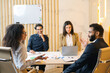 © Face Stock - Multiracial team. Group of ambitious young people in smart casual wear discussing business tasks while sitting at the table in a modern office. Flip chart on the background