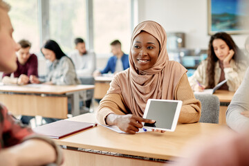 Happy Muslim college student and her classmate use touchpad in classroom.