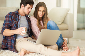 Canvas Print - We do all our shopping online. Shot of a happy young couple using a laptop together while relaxing in their lounge at home.