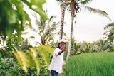 Fototapeta Dziecięca - Half length portrait of excited male tourist waving while laughing and rejoicing during summer vacations trip in Indonesia with rice fields and palm trees, cheerful adult man smiling at camera