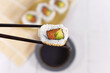 Single sushi inside out roll with salmon, avocado and sesame held by chopsticks