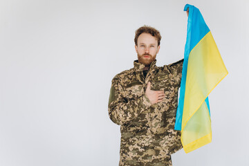 Ukrainian patriot soldier in military uniform holds a hand on a heart with a yellow and blue flag on a white background