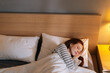 © dikushin - Top view of cute young woman sleeping well in bed hugging soft white blanket at home, bedside lamp lighting with warm yellow light. Charming lady resting enjoying fresh soft bedding linen in bedroom